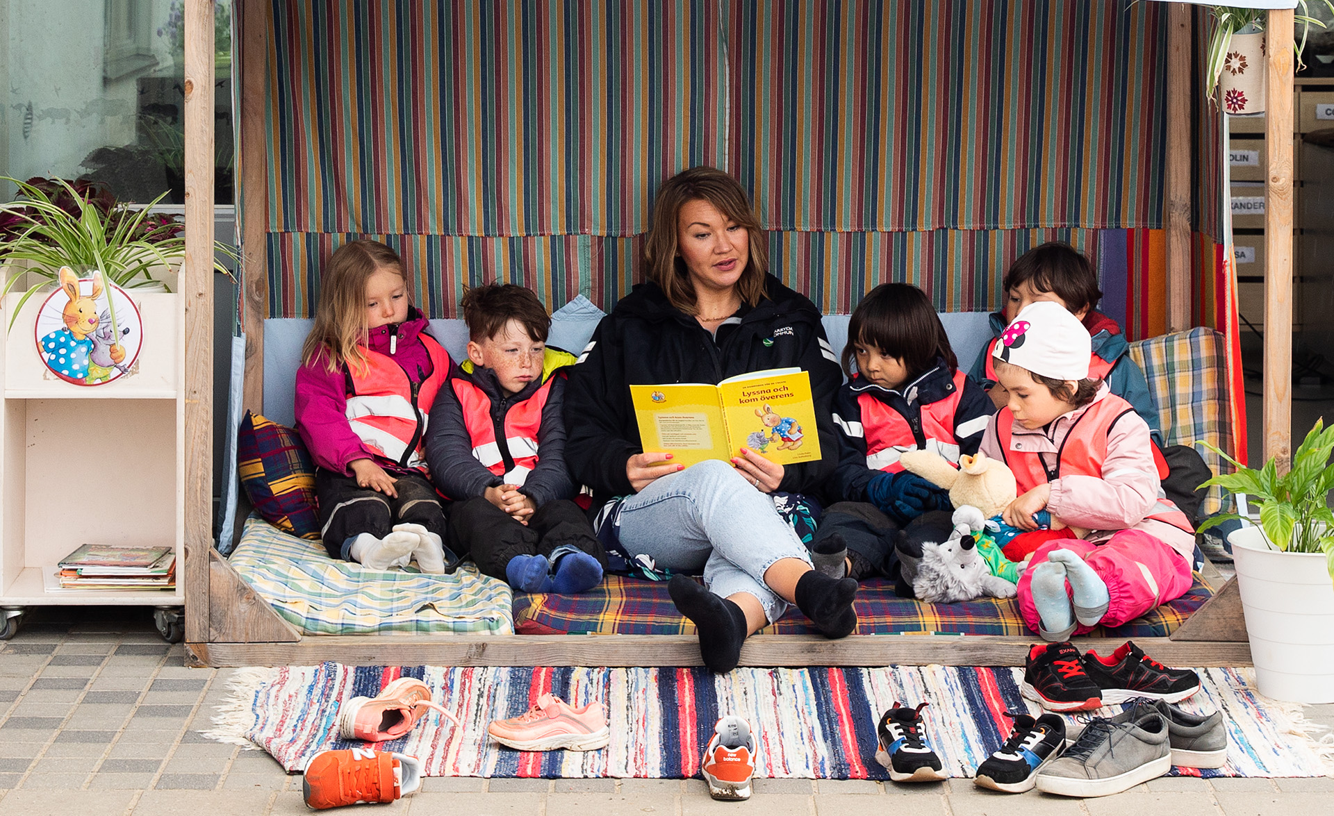 Bild på en grupp barn som sitter och lyssnar när en pedagog läser ur en bok.