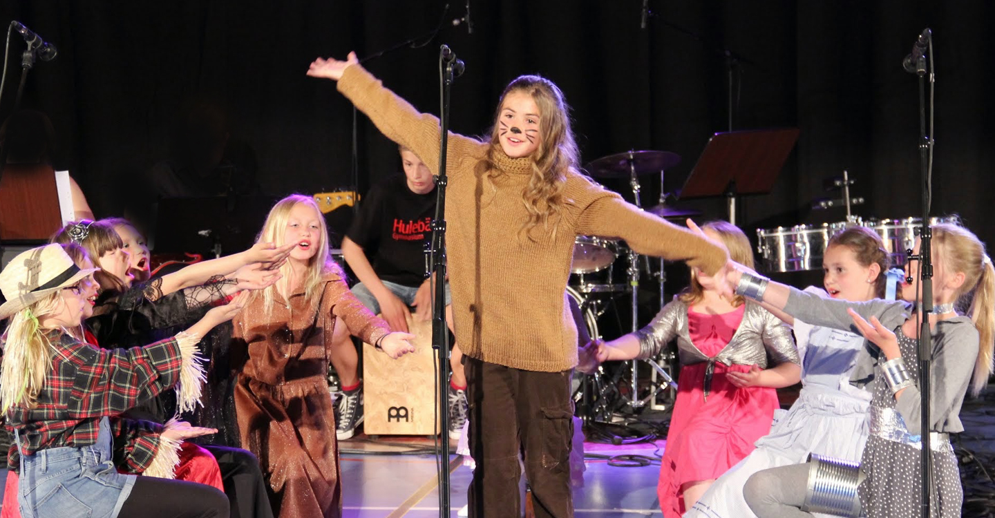 En barnkör som visar en scen ur en föreställning. I mitten av gruppen står en flicka utklädd till mus.