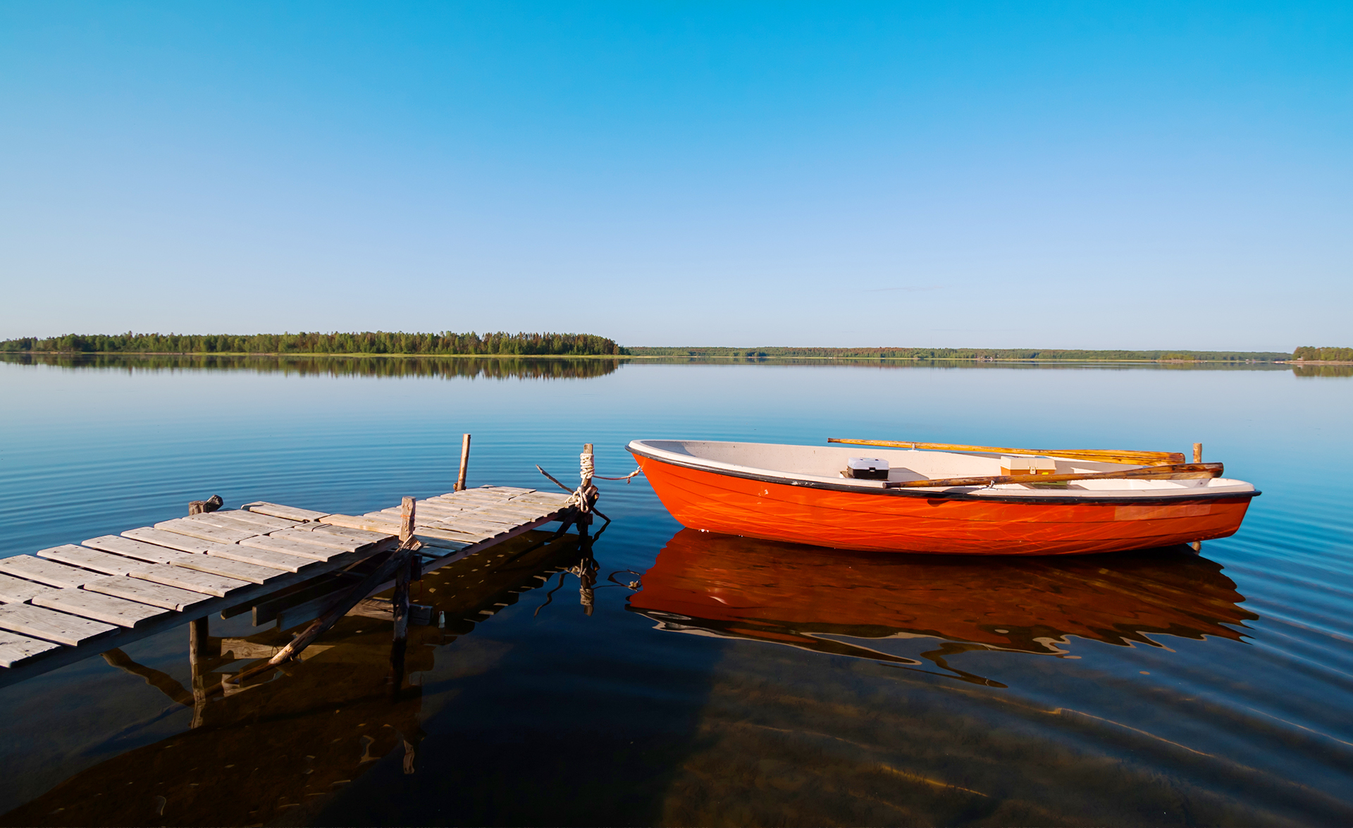 En båt är förankrad i en brygga med ett löst rep. Vattnet är klart och vindstilla i sjön.