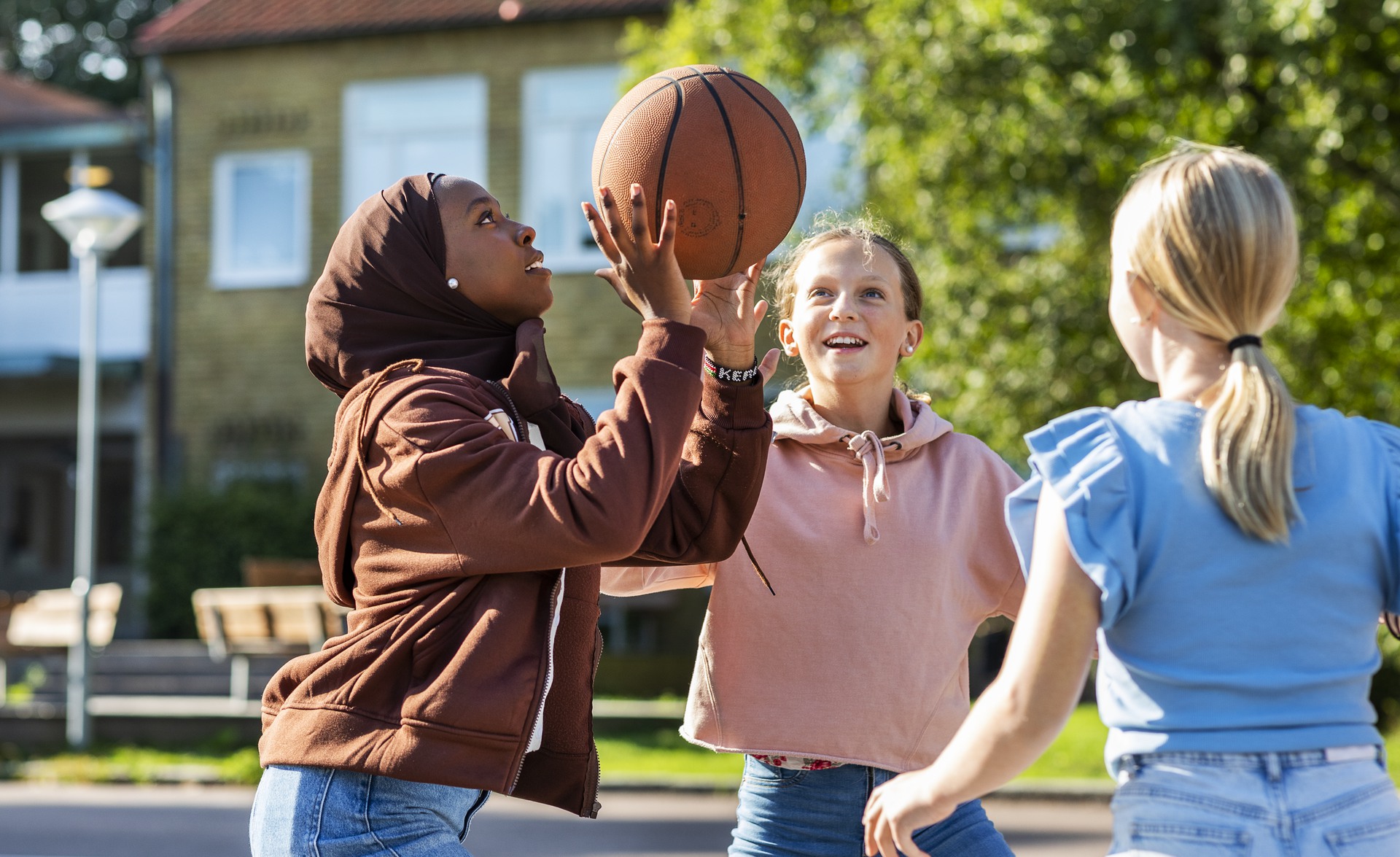 Tre flickor spelar basket på skolgården