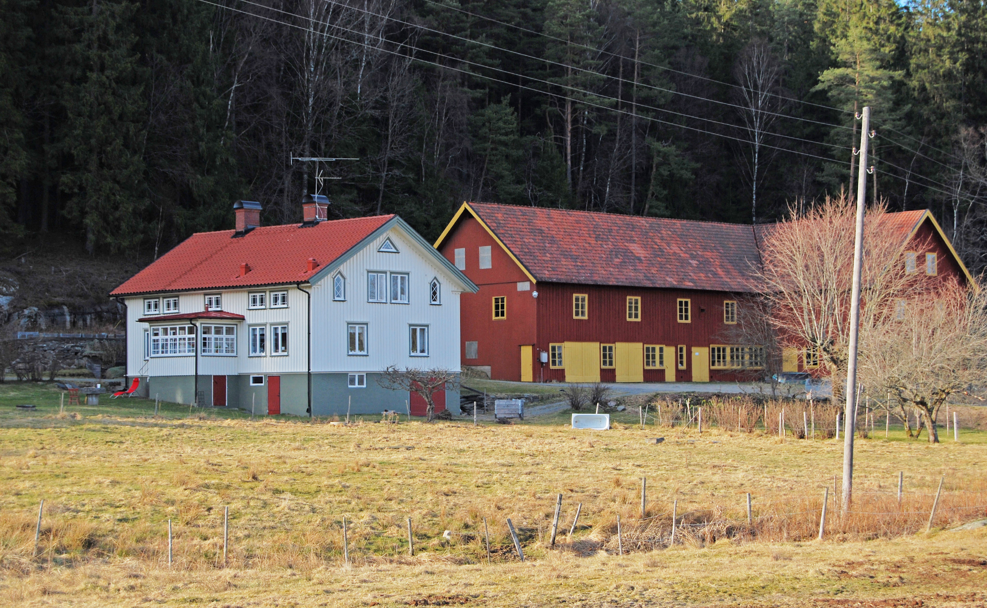 Äldre vitt boningshus och röd ladugård med gula fönsterbågar och portar. 