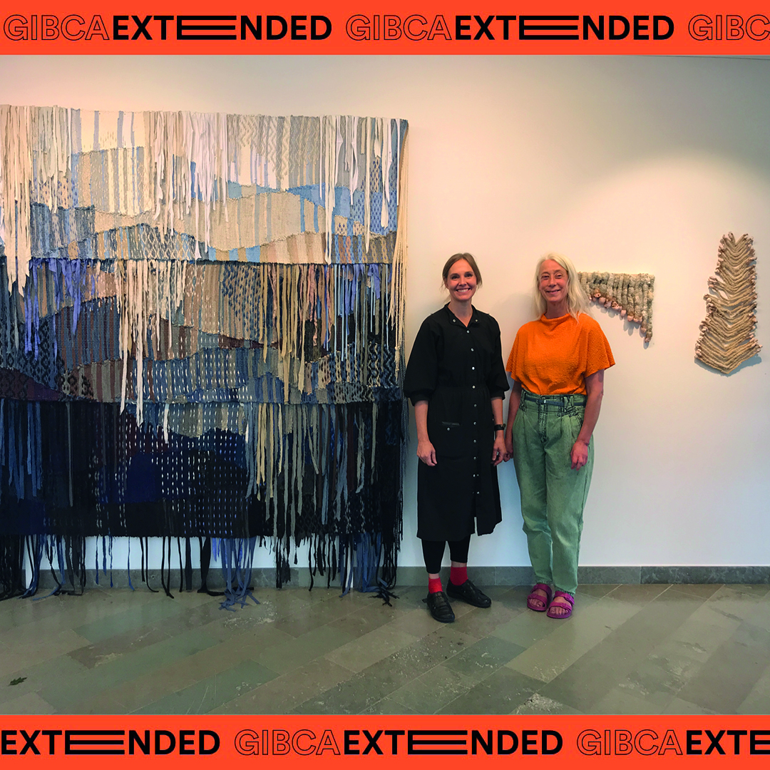 Två kvinnor står fram en en vägg med textila konstverk. Bilden är inramad med texten "GIBCA Extended".